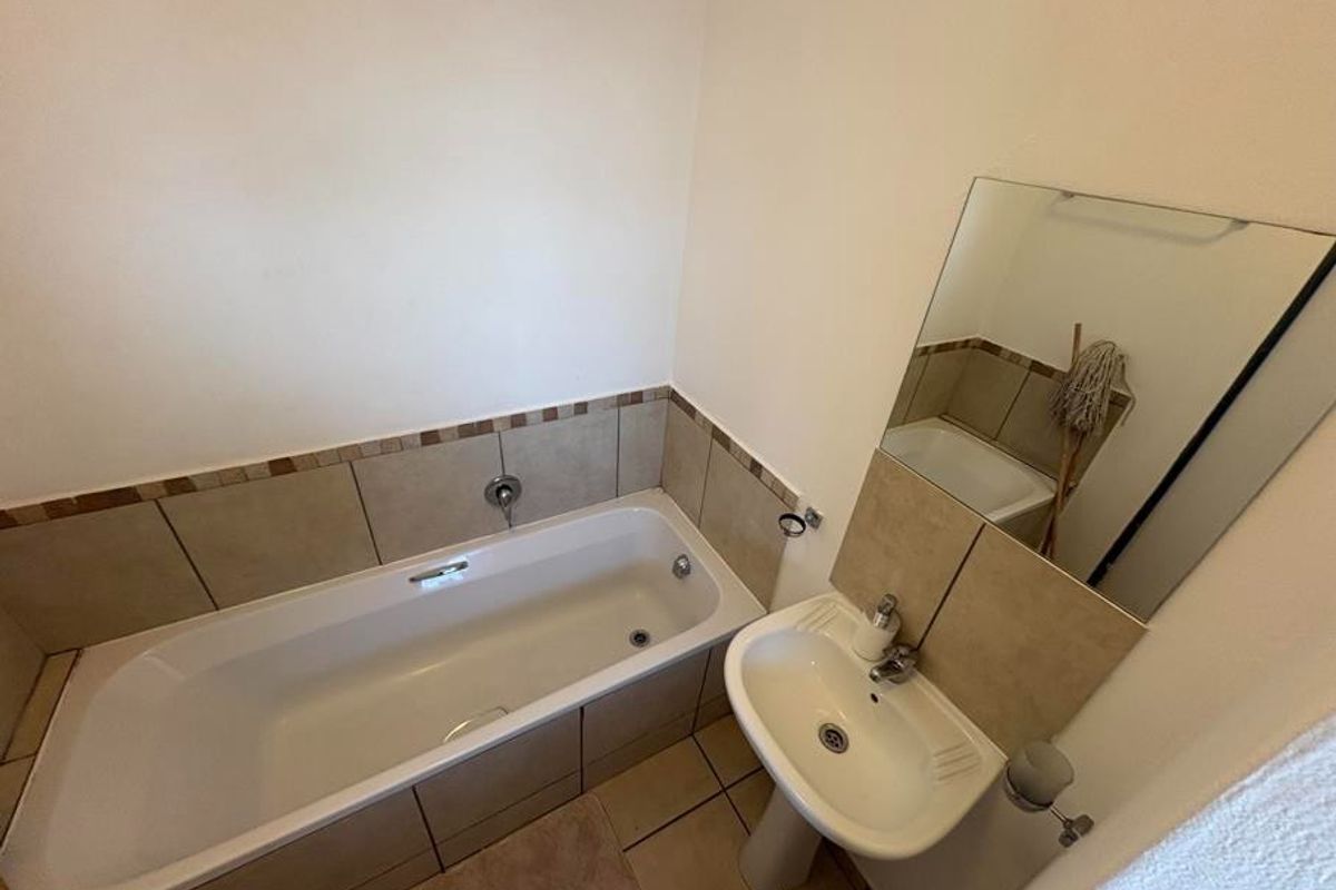 A functional bathroom featuring a standard bathtub, pedestal basin, and wall-mounted mirror with neutral tiled splashbacks.
