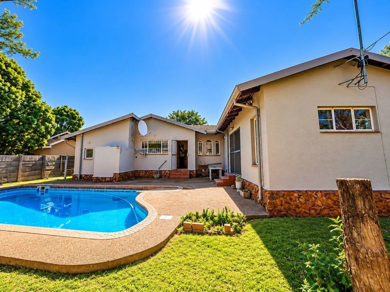 Rear exterior view of the house featuring a swimming pool, paved patio area, and stone-clad foundation walls.