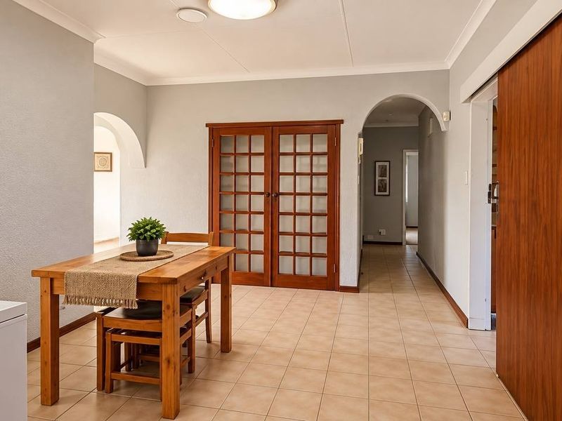 A bright living area featuring tiled flooring, classic archways, and wooden french doors, providing a neutral and functional space with good natural flow.