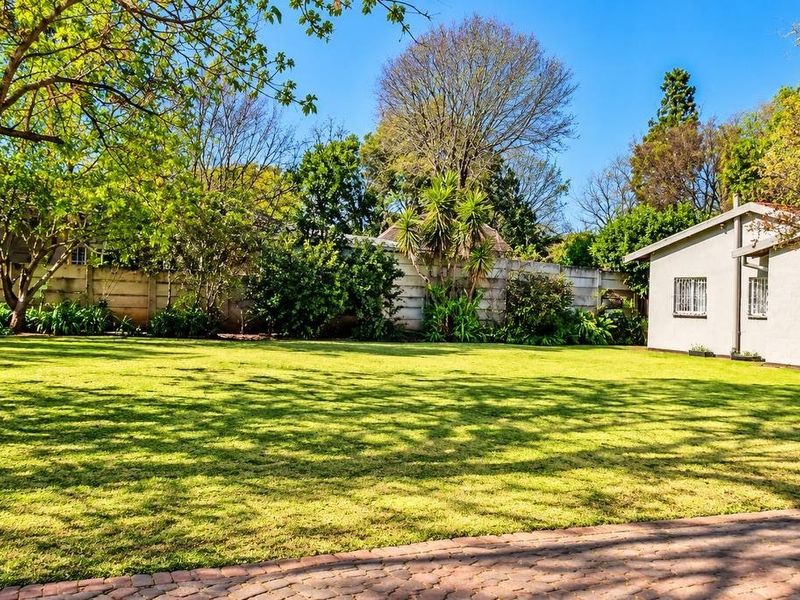 Spacious rear garden featuring a well-maintained lawn, mature trees, and a paved area adjacent to the property structure with secure window fixtures.