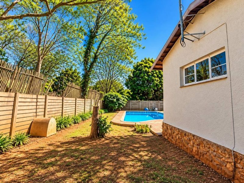 Rear garden area featuring a swimming pool, paved surround, stone-clad exterior wall, and perimeter timber fencing.