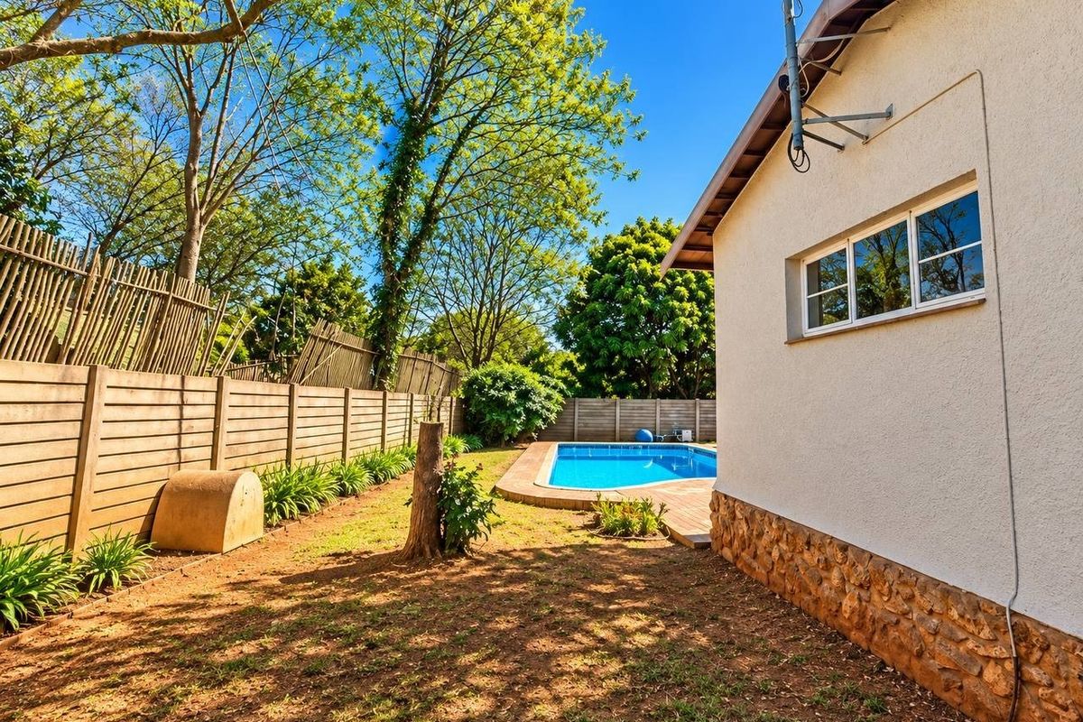 Rear garden area featuring a swimming pool, paved surround, stone-clad exterior wall, and perimeter timber fencing.