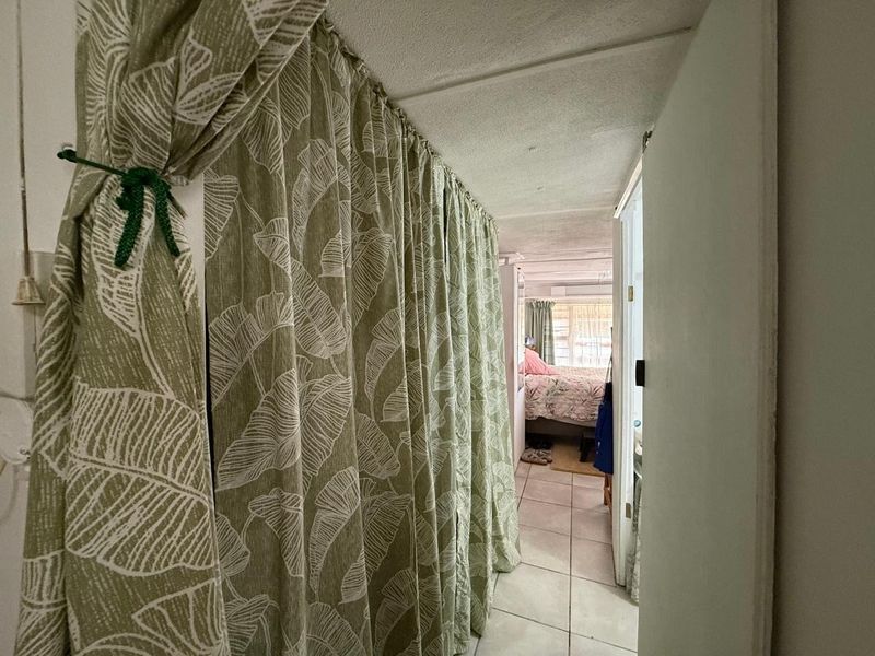 A narrow hallway featuring tiled flooring and a curtain partition, leading into an adjacent bedroom area with visible ceiling wear.