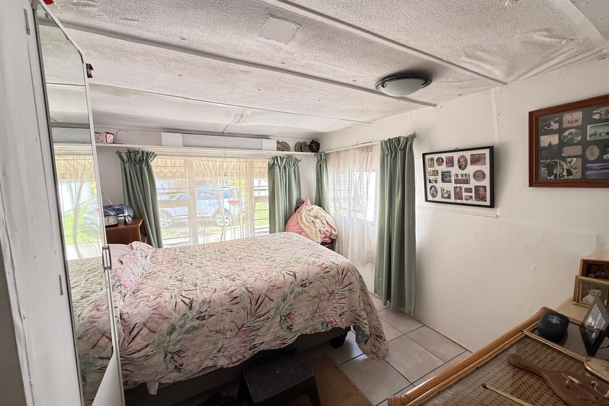 A bedroom featuring tiled flooring, a textured ceiling, and large windows allowing natural light. The space requires cosmetic updates to improve its overall condition.