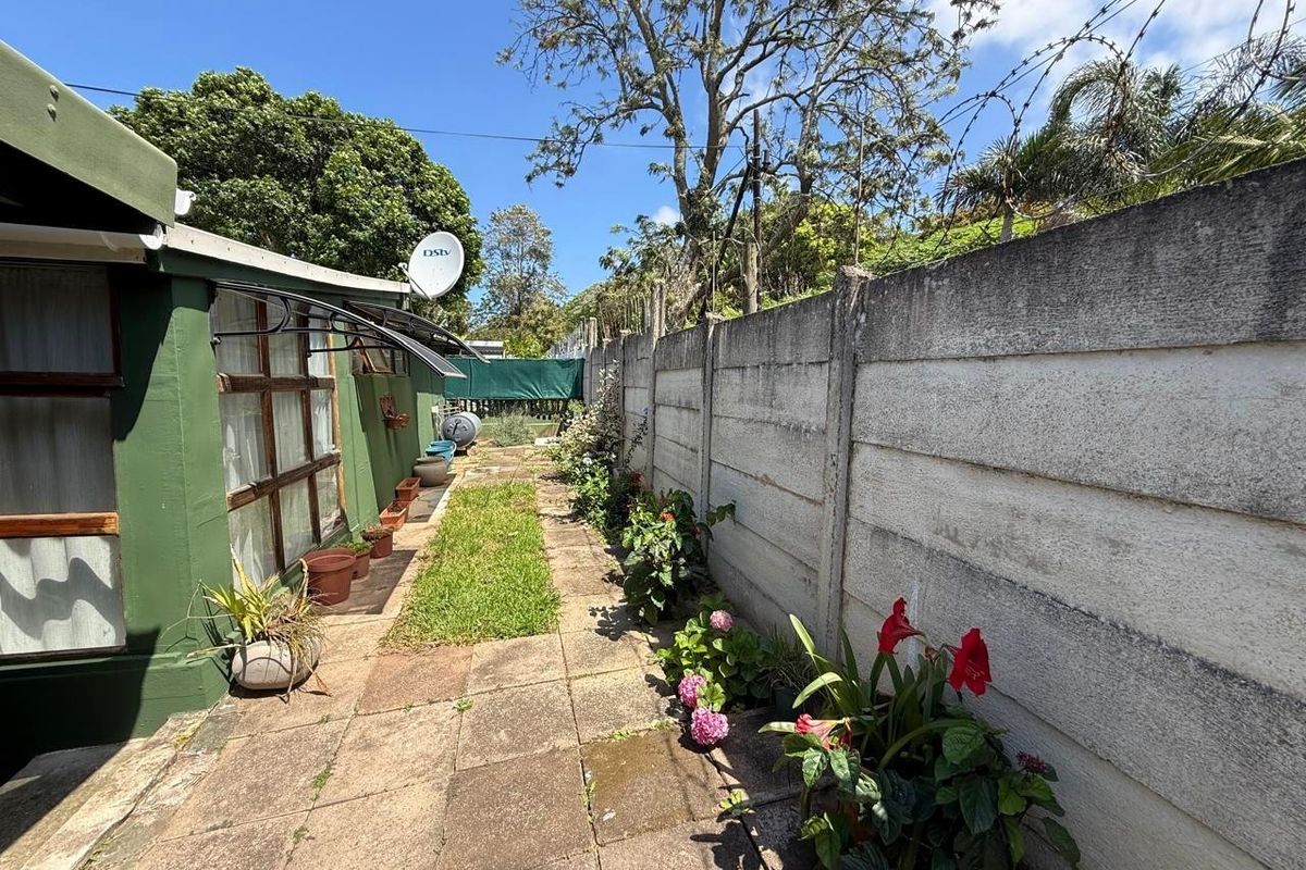 A narrow rear exterior area featuring a paved walkway, a precast concrete boundary wall with security wire, and an attached awning.