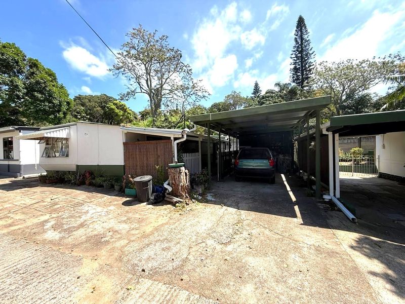 Front exterior view of the townhouse featuring a concrete driveway and a covered carport structure with visible signs of wear.