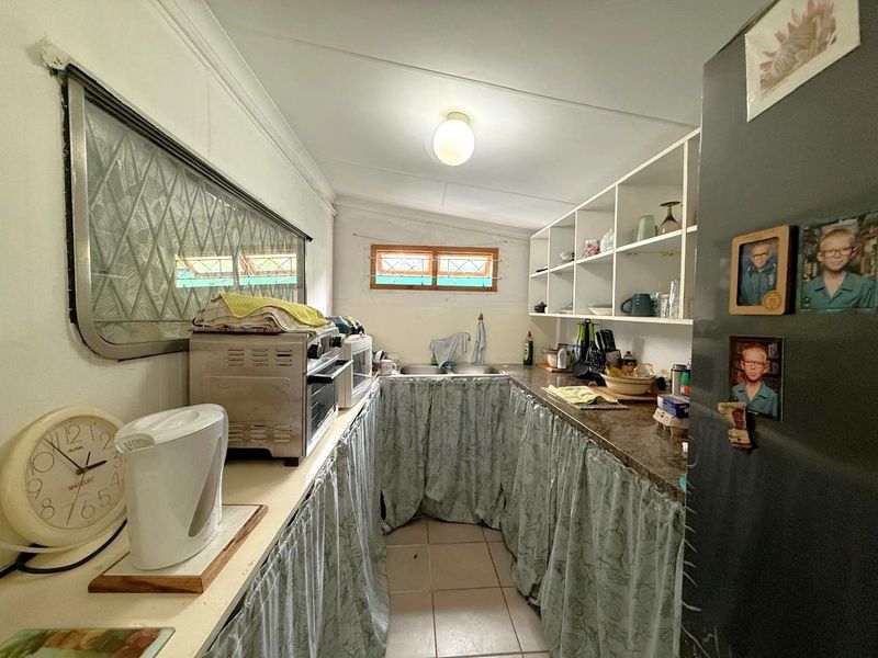 A compact kitchen featuring laminate countertops, double basin sink, open shelving, and tiled flooring, currently utilizing fabric curtains for lower cabinet storage.