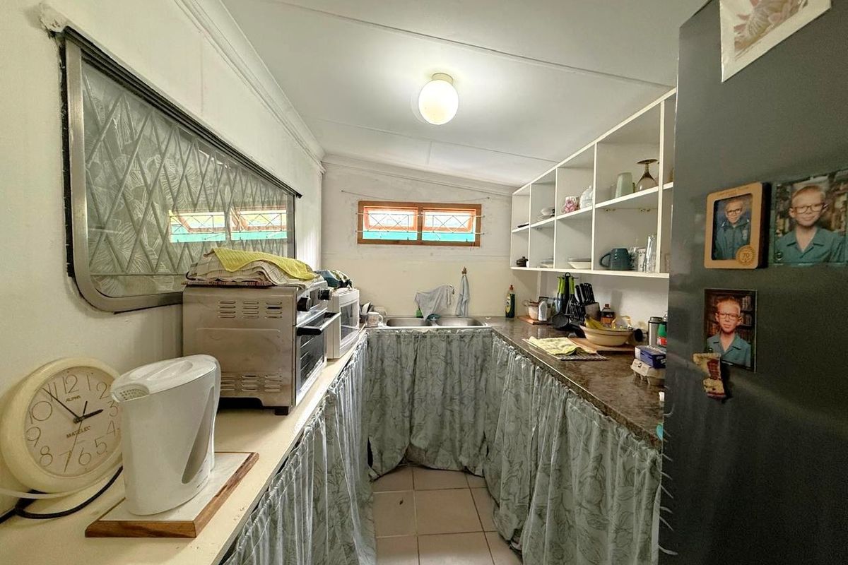 A compact kitchen featuring laminate countertops, double basin sink, open shelving, and tiled flooring, currently utilizing fabric curtains for lower cabinet storage.