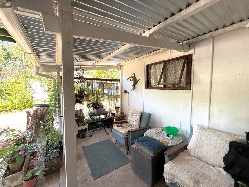 A covered outdoor patio area featuring a corrugated metal roof, timber support posts, and concrete flooring, offering a functional space for outdoor relaxation.