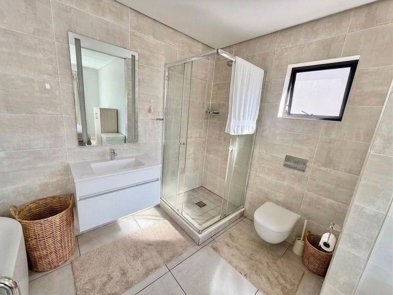 Modern bathroom featuring a wall-mounted vanity with integrated basin, glass shower enclosure, and wall-hung toilet, finished with neutral floor-to-ceiling tiling.