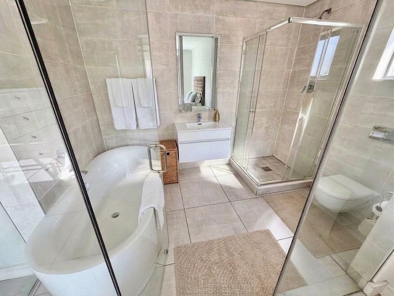 Modern bathroom featuring a freestanding bathtub, separate glass shower enclosure, wall-mounted vanity with basin, and wall-mounted toilet with neutral tiled finishes.