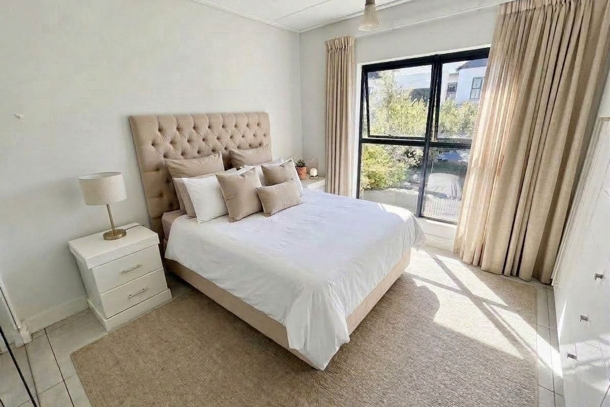 A well-lit bedroom featuring tiled flooring and a large black aluminium window frame, providing natural light and a pleasant outlook.