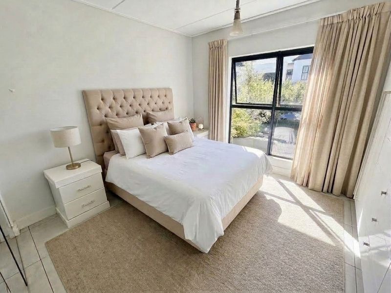 A well-lit bedroom featuring tiled flooring and a large black aluminium window frame, providing natural light and a pleasant outlook.
