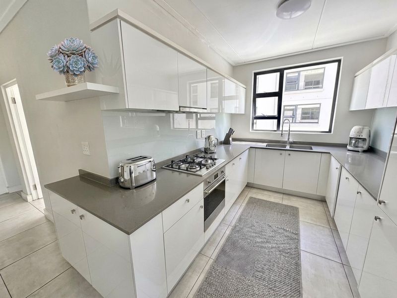 Modern kitchen featuring sleek white cabinetry, stone countertops, integrated gas hob, oven, and a glass splashback with ample natural light.
