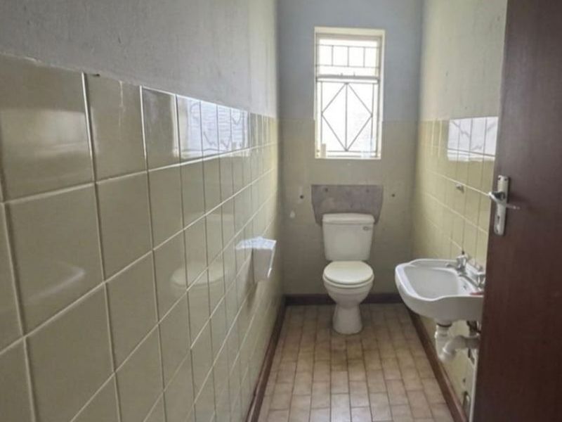 A compact, dated bathroom featuring a toilet, wall-mounted basin, and original ceramic wall tiling, requiring cosmetic updates to modernize the space.