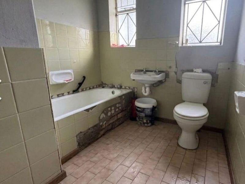 A dated bathroom featuring a bathtub, wall-mounted basin, and toilet, currently requiring significant renovation and repair to the wall finishes and tiling.