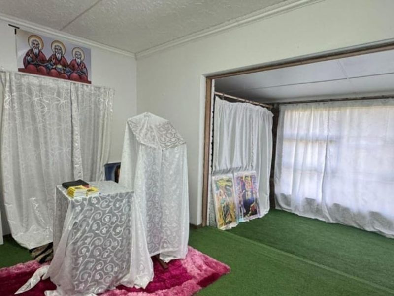 A living area featuring a large window opening and coved ceilings, currently utilized as a prayer space with synthetic grass flooring.