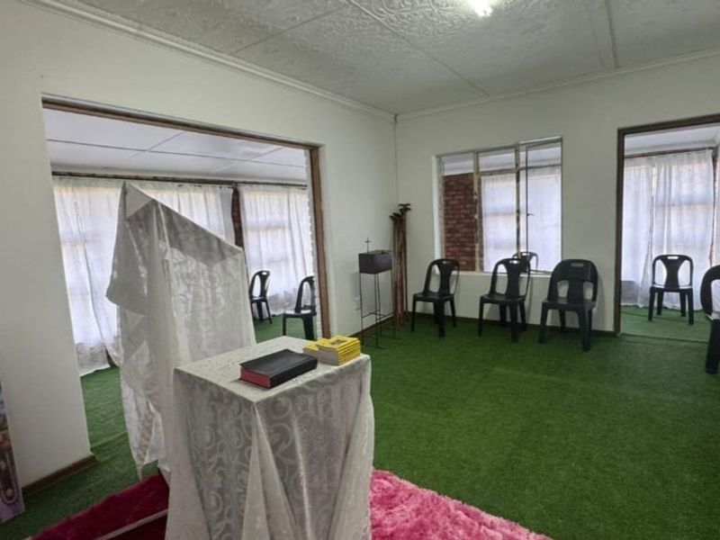A multi-room living area featuring pressed metal ceilings and large windows, currently utilized as a communal space with artificial grass flooring.