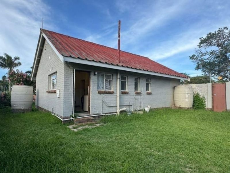 Rear view of a detached house featuring a corrugated metal roof, brick exterior walls, and external water storage tanks set within a grassed garden area.