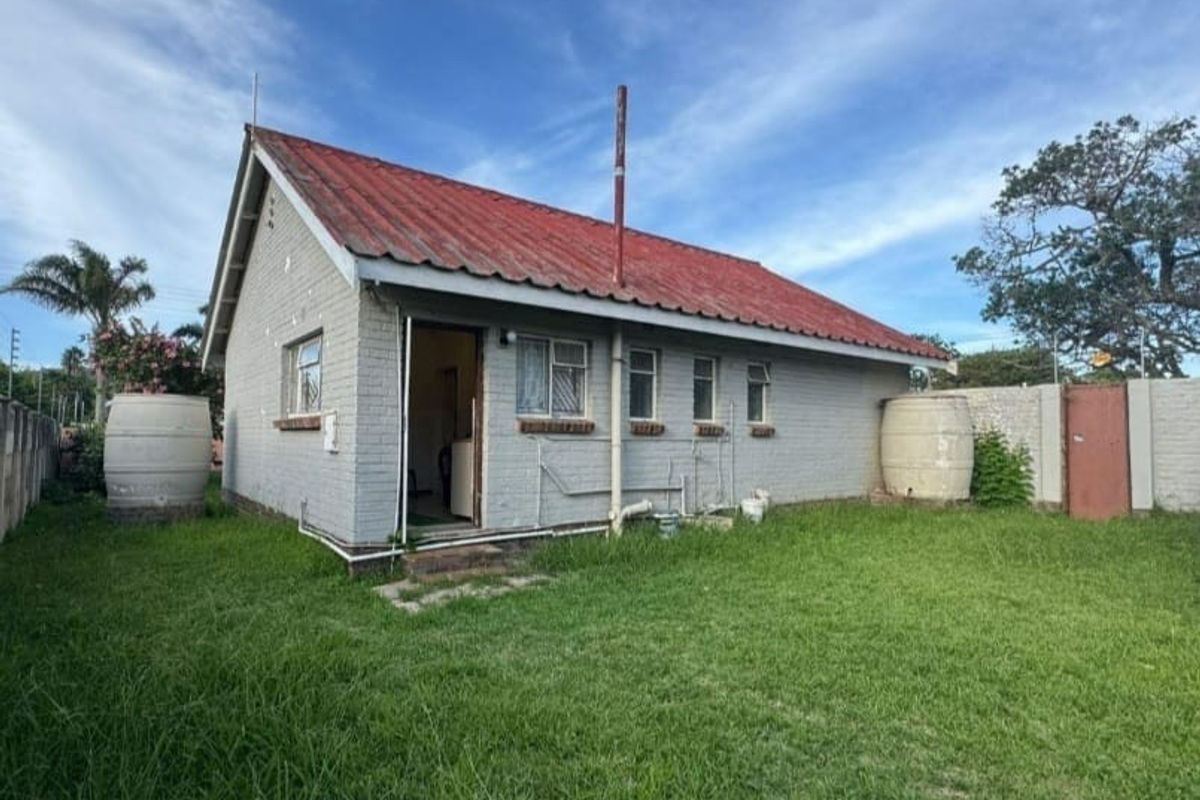 Rear view of a detached house featuring a corrugated metal roof, brick exterior walls, and external water storage tanks set within a grassed garden area.