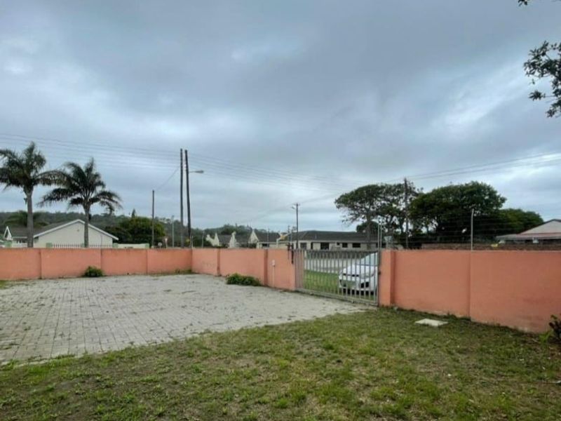 A rear outdoor area featuring a paved driveway, perimeter wall, and metal gate access, providing a functional space for parking or outdoor use.