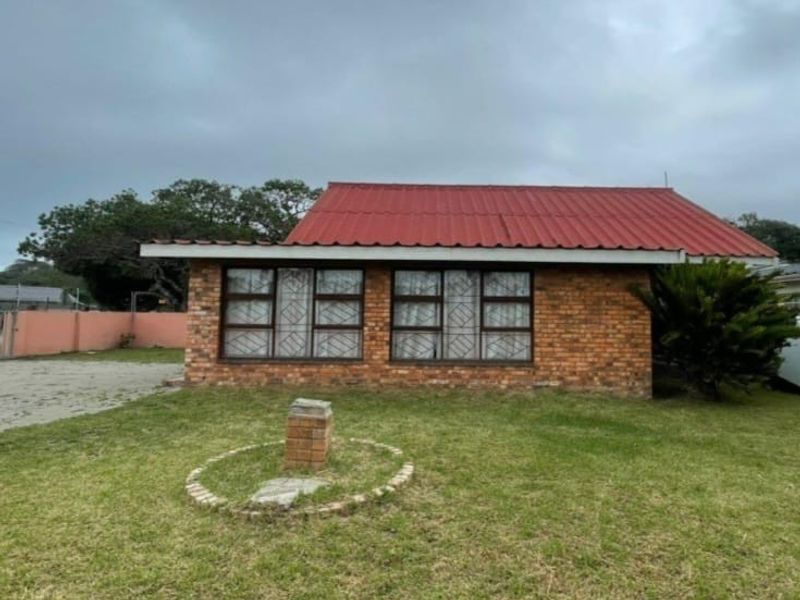 A single-story face brick house featuring a red corrugated metal roof, aluminum windows with security bars, and a front lawn with a brick pillar.