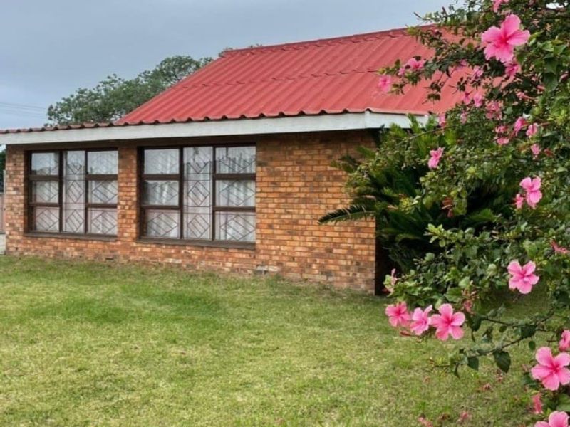 A view of the rear exterior of the house featuring a brick facade, corrugated metal roof, and security-barred windows overlooking a lawn.