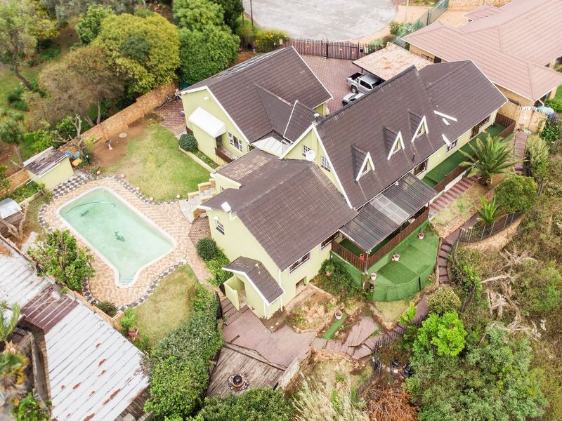 Aerial view of a residential property featuring a swimming pool, tiled roof, paved driveway, carport, and landscaped garden areas.