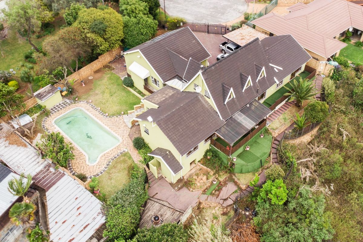 Aerial view of a residential property featuring a swimming pool, tiled roof, paved driveway, carport, and landscaped garden areas.