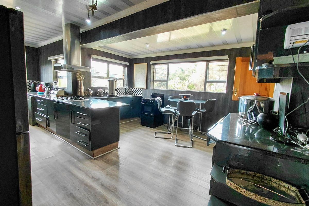 Spacious kitchen featuring dark cabinetry, stone countertops, stainless steel extractor fan, and ample natural light through large aluminium-framed windows.