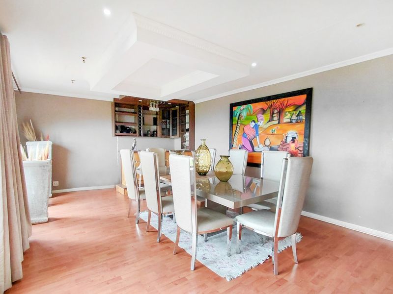 A spacious dining room featuring laminate flooring, a recessed ceiling with downlights, and a built-in bar area.