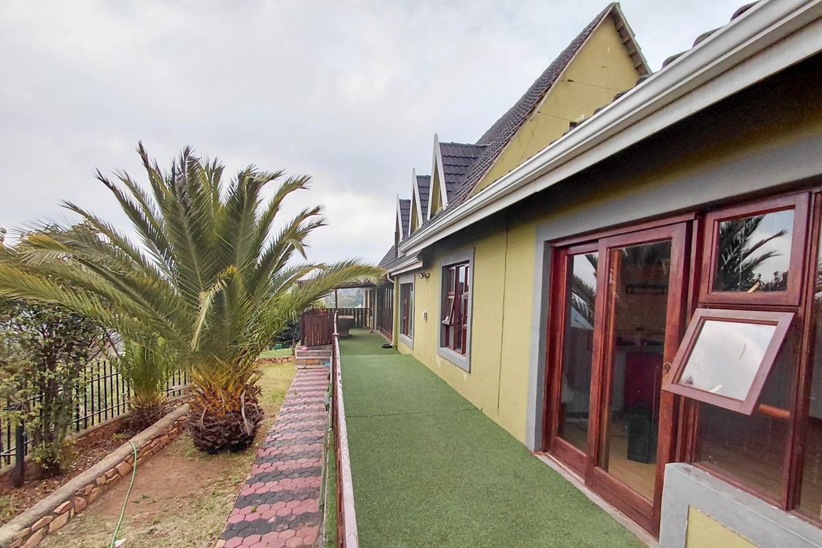 Rear exterior view of the house featuring a paved walkway, artificial lawn, and multiple sliding door access points along the side elevation.