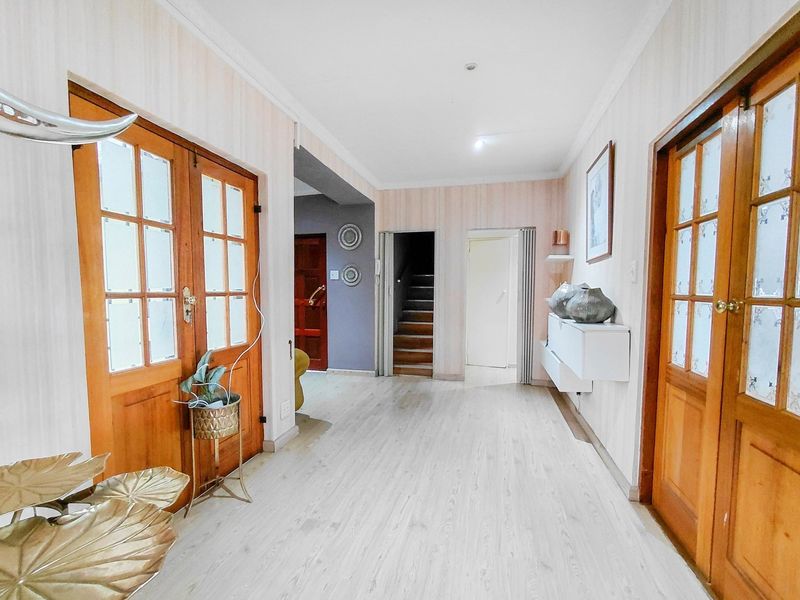 Spacious entrance hallway featuring light-toned laminate flooring, timber-framed glass doors, and access to a staircase.