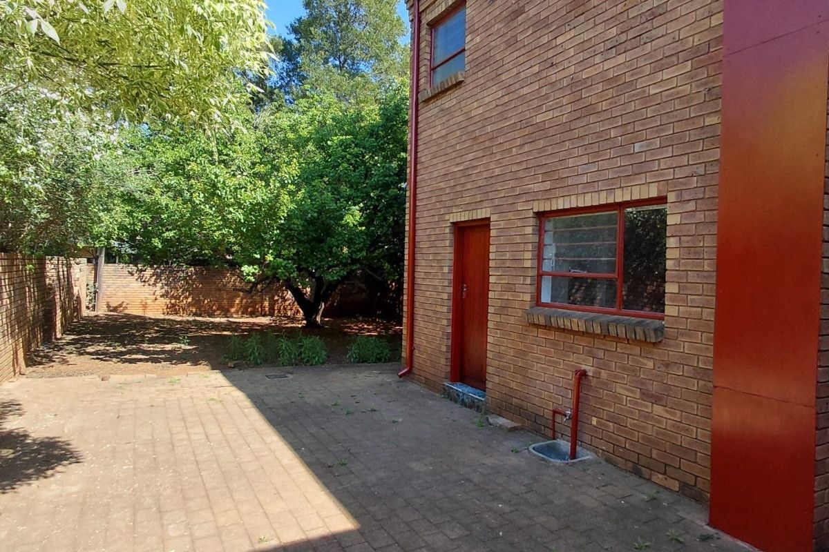 Rear view of the property featuring a brick facade, paved patio area, and established garden with boundary walling.