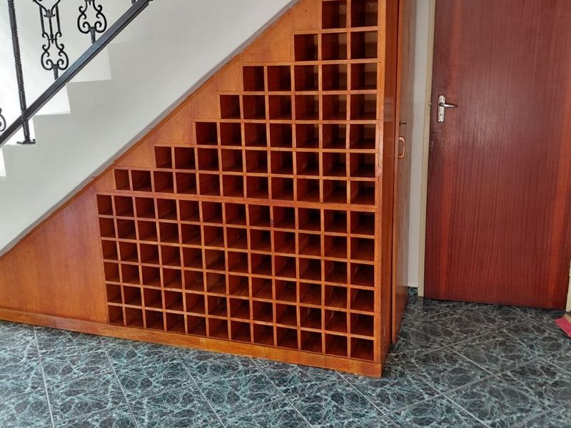 A well-maintained hallway featuring a custom built-in wooden wine rack under the staircase, complemented by decorative wrought iron railings and tiled flooring.