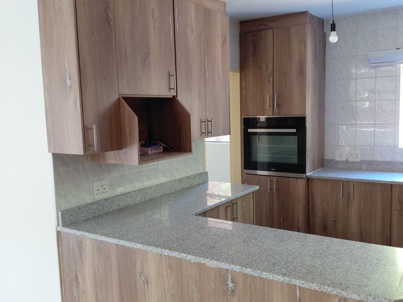 Modern kitchen featuring wood-look cabinetry, granite countertops, a built-in oven, and a tiled backsplash, offering a clean and functional workspace.