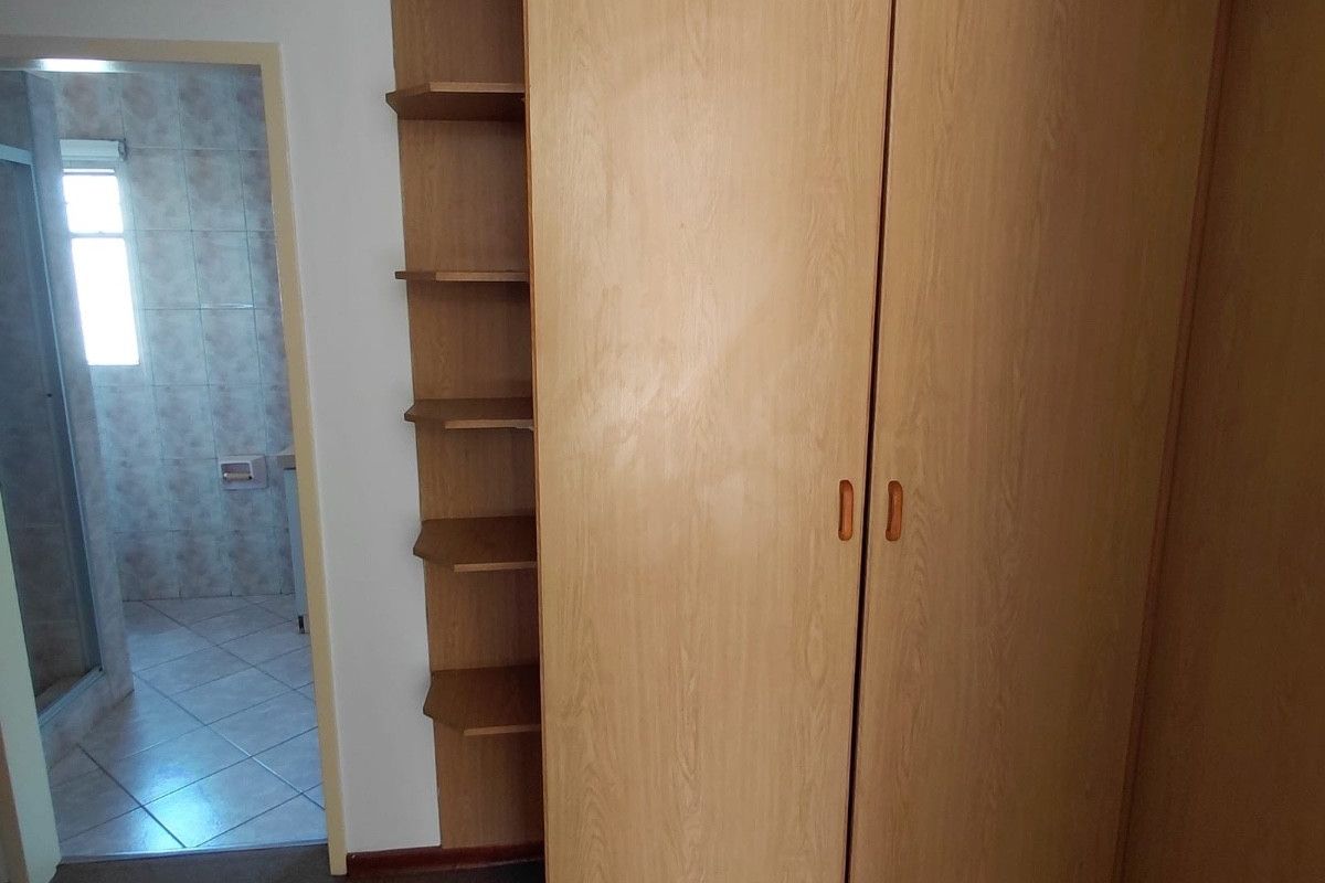 Bedroom featuring built-in wooden wardrobes and integrated shelving, with an adjacent tiled bathroom visible through the doorway.