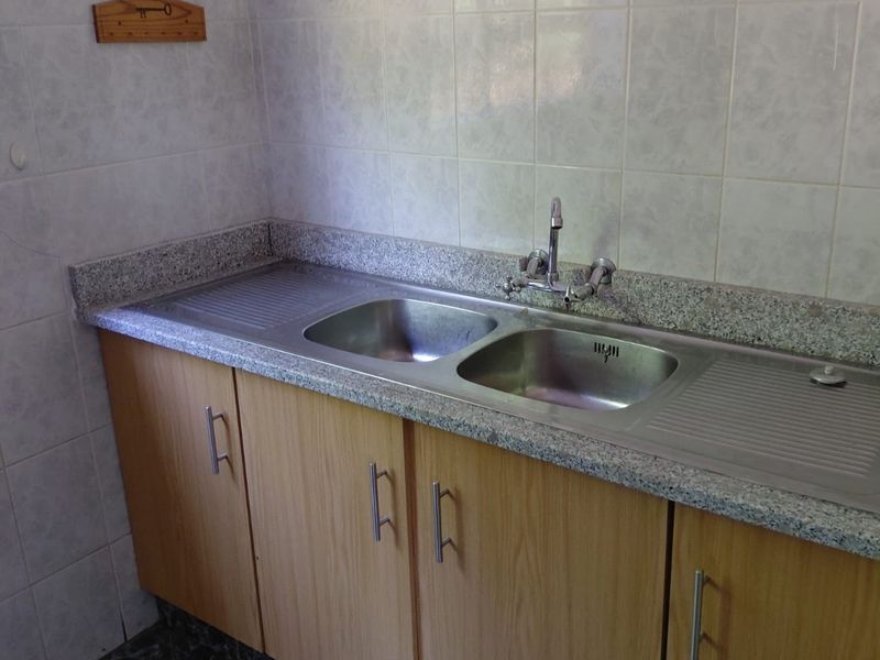 A functional scullery area featuring a double stainless steel sink, granite countertops, and light wood-finish cabinetry with tiled wall and floor finishes.