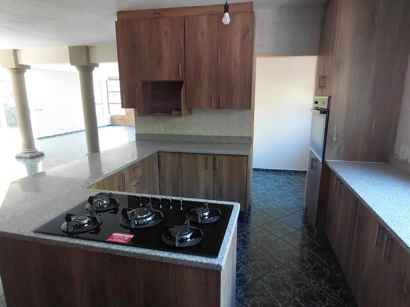 A functional kitchen featuring wood-look cabinetry, granite countertops, a built-in gas hob, and an integrated oven, set against dark tiled flooring.