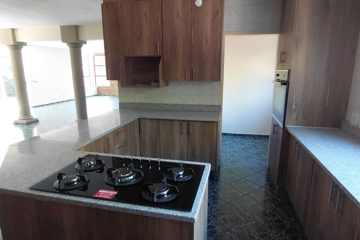 A functional kitchen featuring wood-look cabinetry, granite countertops, a built-in gas hob, and an integrated oven, set against dark tiled flooring.
