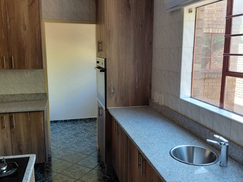 A functional kitchen featuring wood-look cabinetry, granite countertops, a built-in oven, and a stainless steel sink with tiled finishes throughout.
