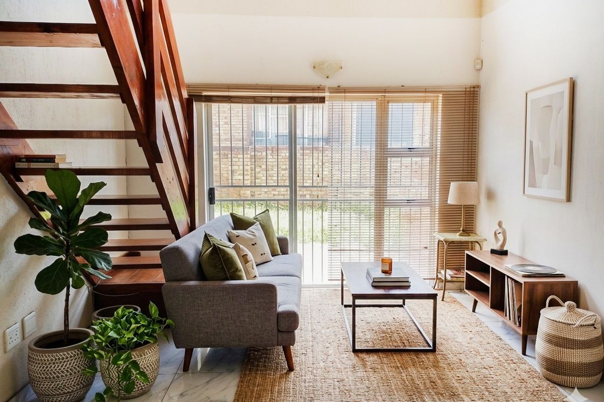 A bright living room featuring a wooden staircase, marble-look flooring, and a sliding glass door with venetian blinds leading to the exterior.