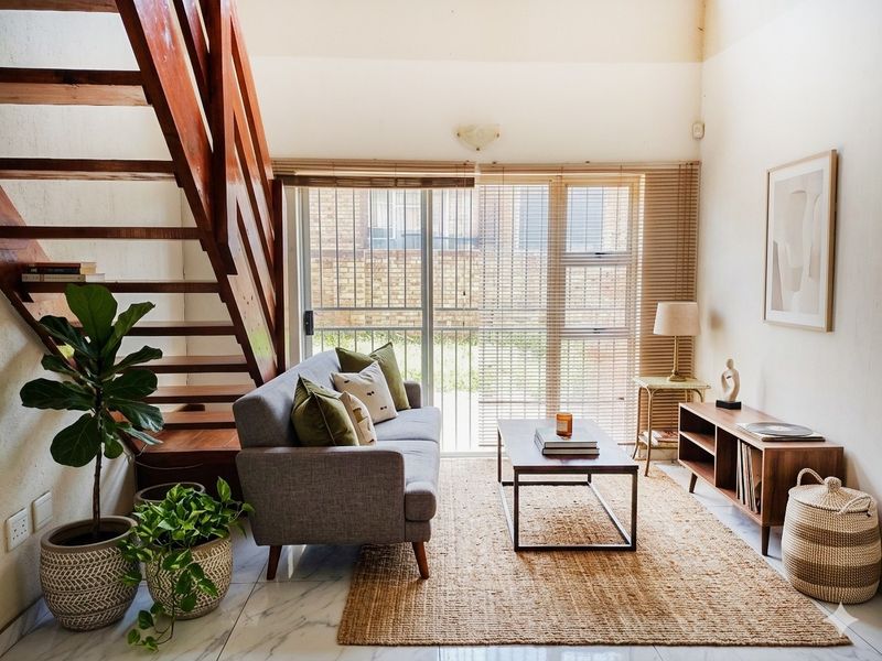 A bright living room featuring a wooden staircase, marble-look flooring, and a sliding glass door with venetian blinds leading to the exterior.