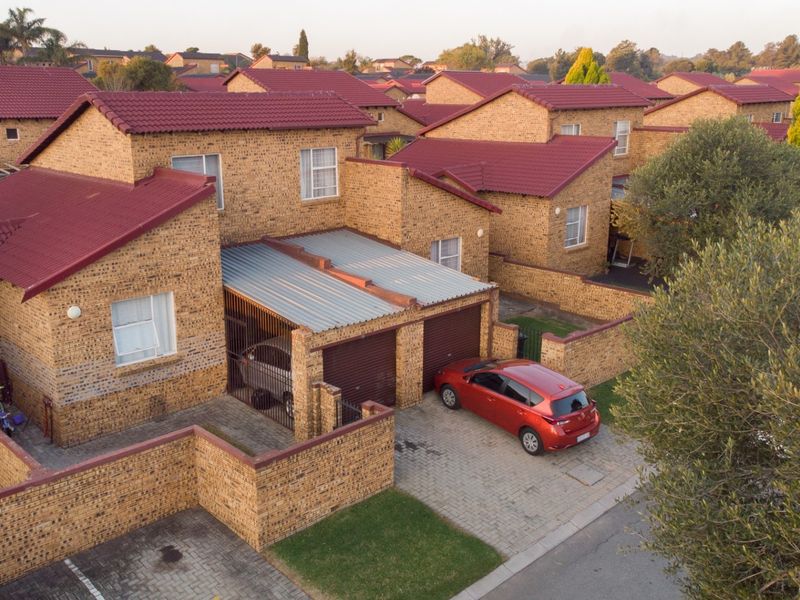 Aerial view of a residential complex featuring face brick houses with red tiled roofs, paved driveways, and secure garage access.