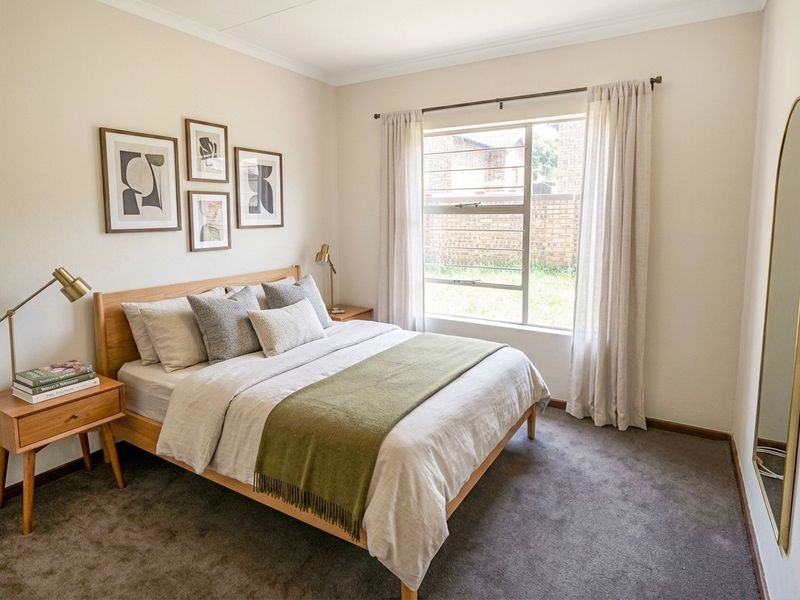 A well-maintained bedroom featuring neutral wall tones, plush carpeting, and a large window that provides natural light.