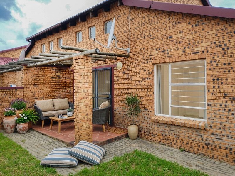 A charming outdoor patio area featuring a timber pergola, exposed brickwork, and tiled flooring, providing a comfortable space for relaxation.
