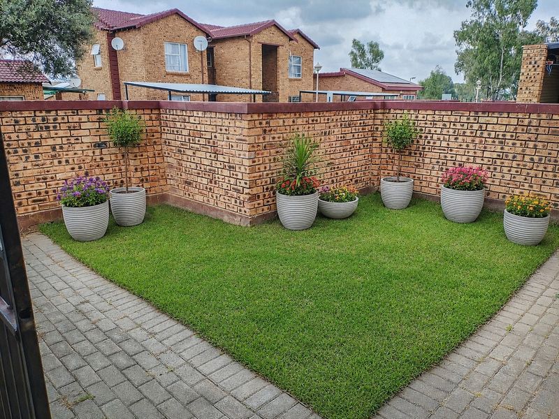 A well-maintained private garden area featuring a neat lawn, paved pathways, and a sturdy face brick boundary wall.