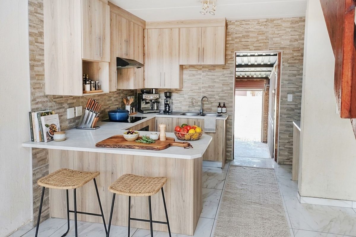 Modern kitchen featuring light-wood cabinetry, stone-look backsplash, marble-effect floor tiles, and a functional breakfast bar with integrated hob and sink.