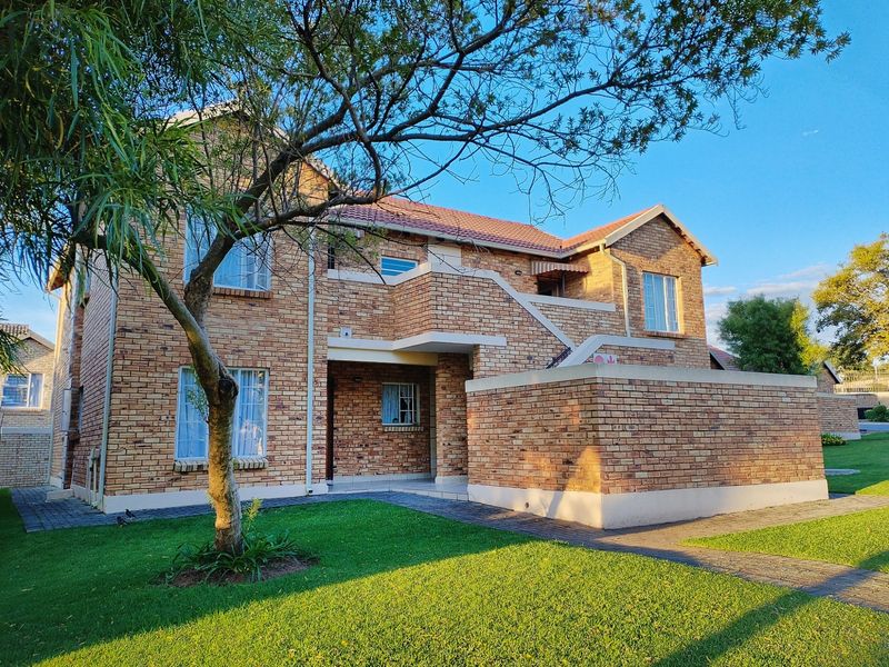 A well-maintained face brick apartment building exterior featuring a tiled roof, paved walkways, and an external staircase set within a landscaped garden.
