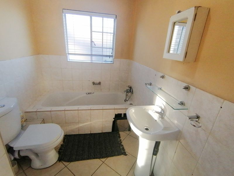 A functional bathroom featuring a bathtub, pedestal basin, and toilet, with tiled finishes and a window for natural light.
